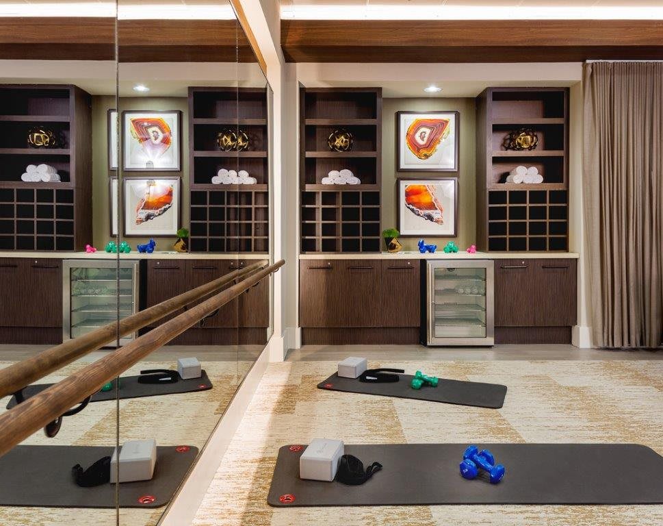 A well-equipped exercise room with yoga mats, yoga blocks, resistance bands, mirrors, and colorful artwork on the shelves.