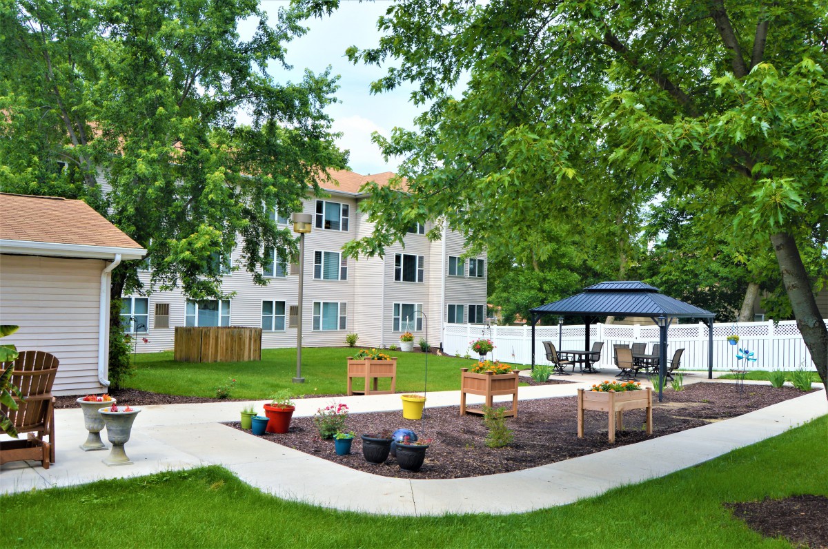 A serene outdoor garden area with benches and a gazebo, adjacent to a residential building.