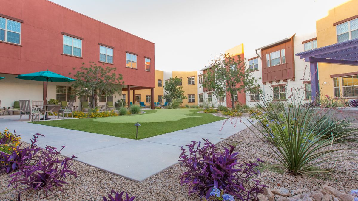 A modern courtyard surrounded by colorful apartment buildings, featuring landscaped green spaces and vibrant foliage.