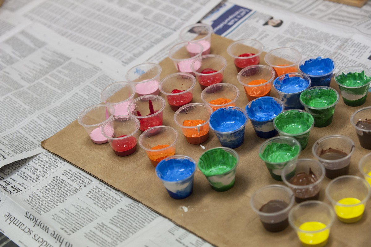 A collection of colorful paints in small containers arranged on cardboard.