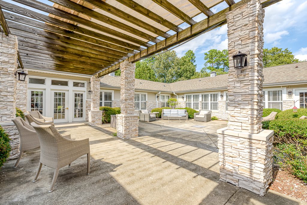 A spacious patio with a wooden pergola and stone columns, featuring outdoor seating and lush landscaping.