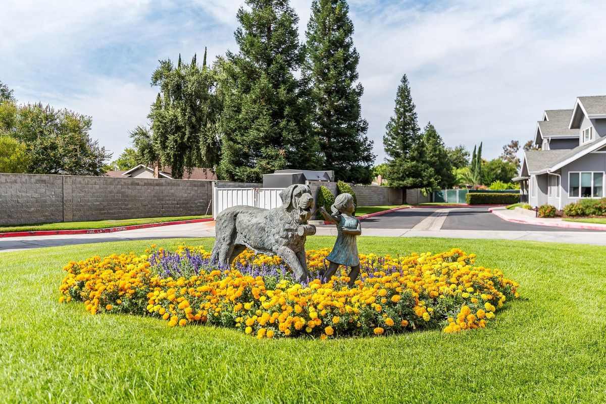 A sculpture of a child with a lamb surrounded by vibrant yellow flowers in a landscaped garden.