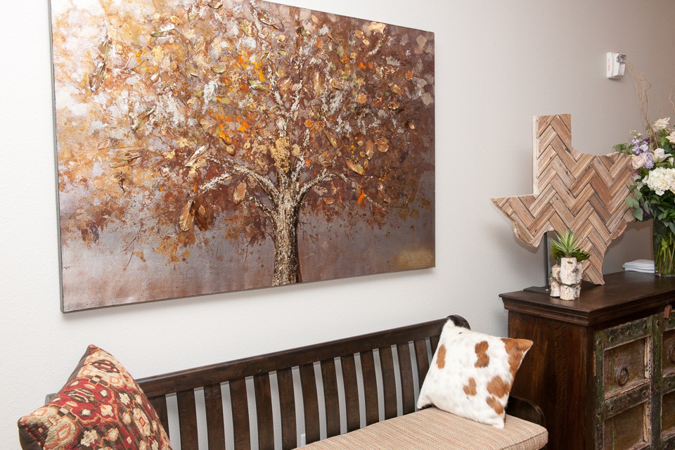 A room with a bench and cushions, featuring a large painting of a tree in autumn colors on the wall.
