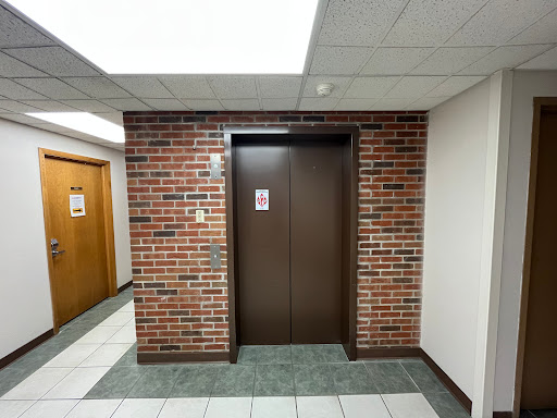 An elevator entrance located between brick and tiled walls in a building hallway.