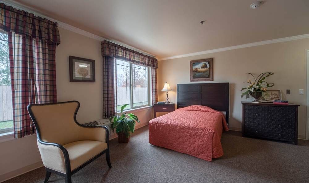 A cozy bedroom featuring a single bed, armchair, and a large window with elegant curtains.