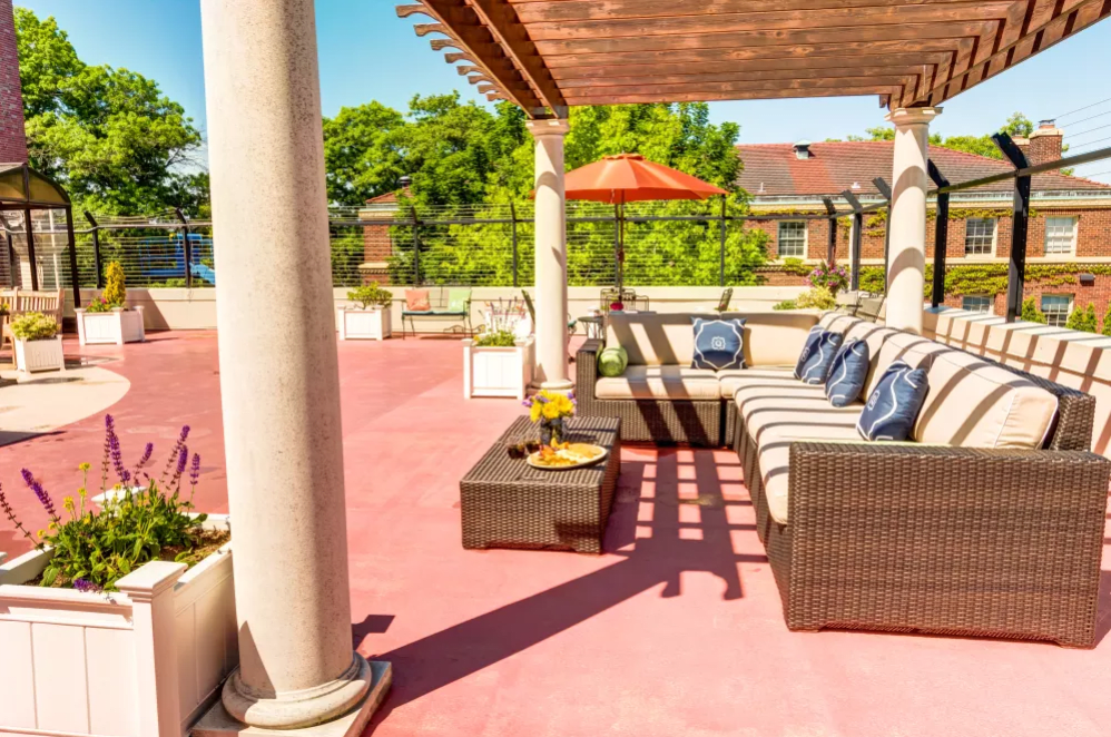 A sunny patio with comfortable outdoor seating under a pergola, featuring cozy cushions and a vibrant umbrella.