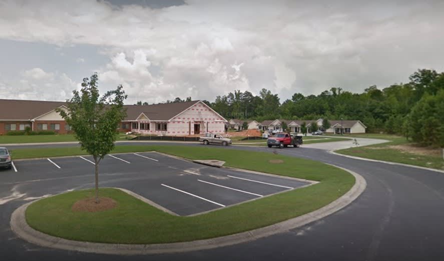 A small building with a parking lot, surrounded by trees under a cloudy sky.