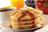 A stack of pancakes drizzled with syrup, accompanied by coffee and orange juice.