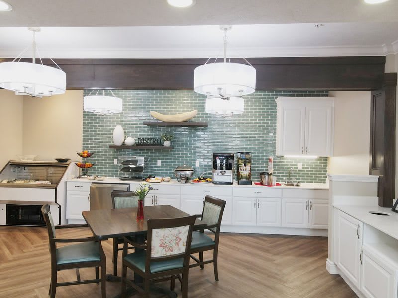 A modern kitchen and dining area featuring white cabinets, a tile backsplash, wood flooring, and elegant light fixtures.