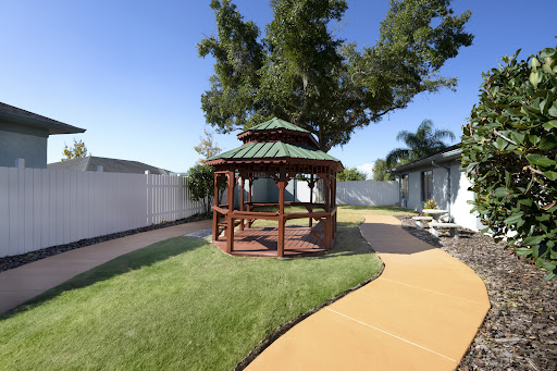 A serene outdoor garden featuring a wooden gazebo surrounded by lush grass and a winding pathway.