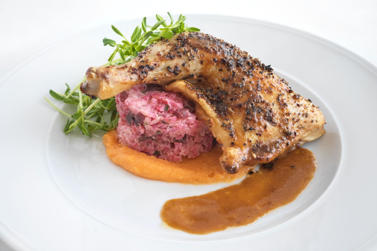 A gourmet dish featuring seasoned chicken atop a bed of minced meat and garnished with fresh herbs, presented with a rich sauce.