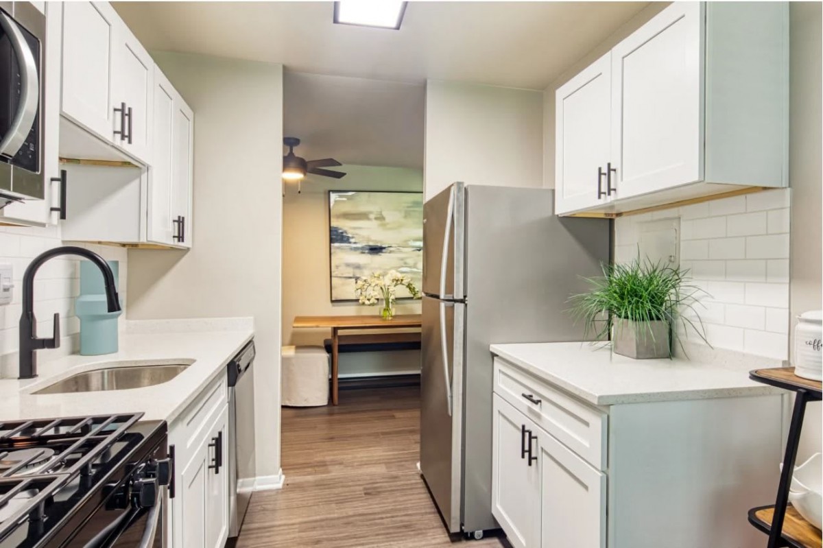 A modern apartment kitchen with white cabinets and stainless steel appliances.