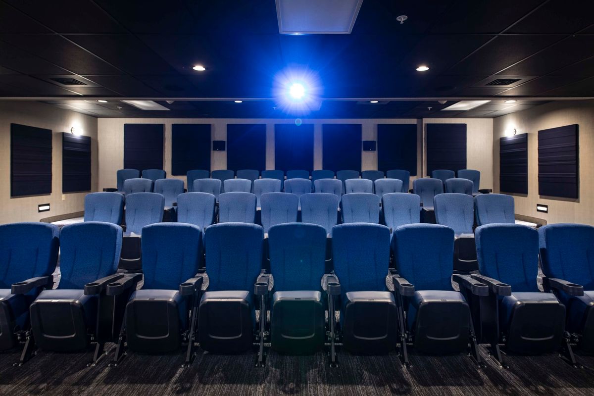 An empty cinema with rows of blue seats and a lit projector.