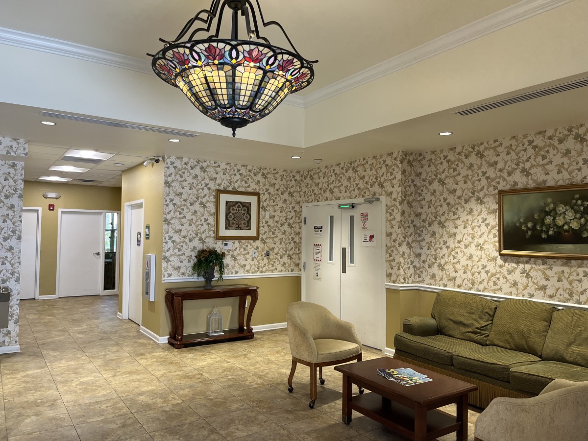 A cozy lobby area with floral wallpaper, a sofa set, and a decorative chandelier.