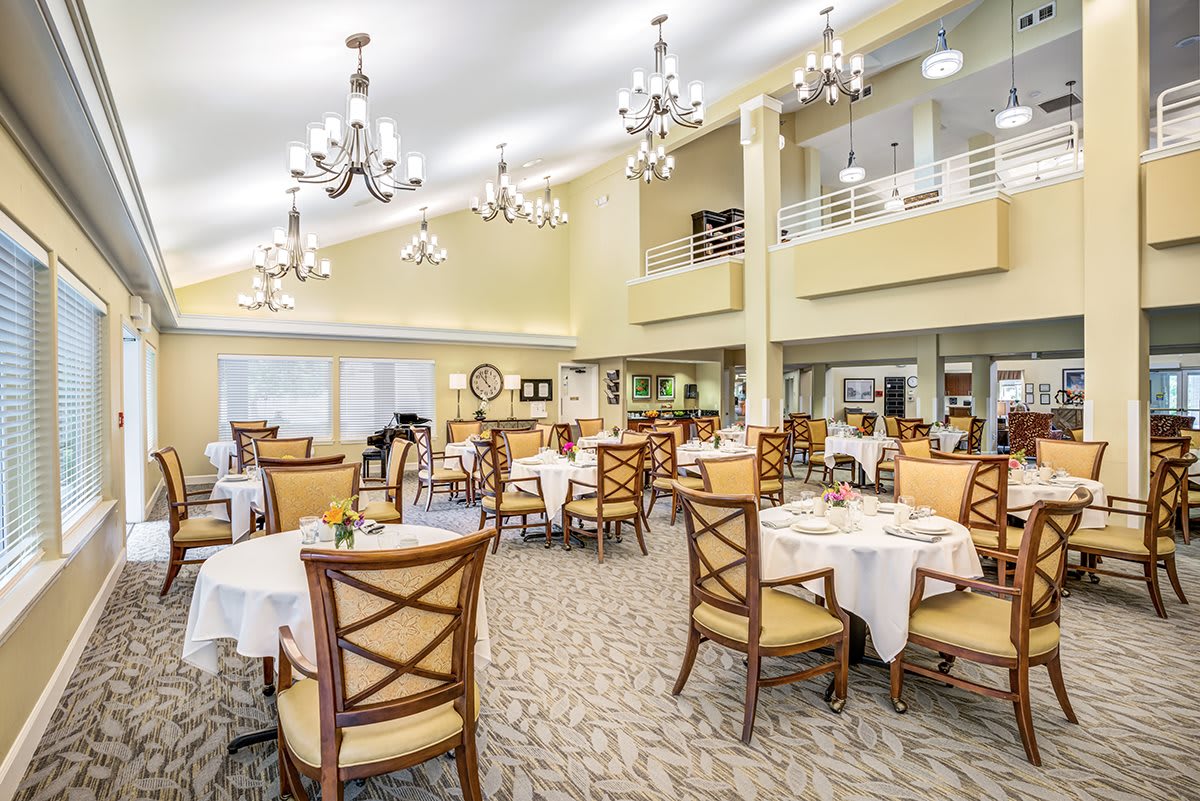 An elegant dining room with tables and chairs arranged under chandeliers.