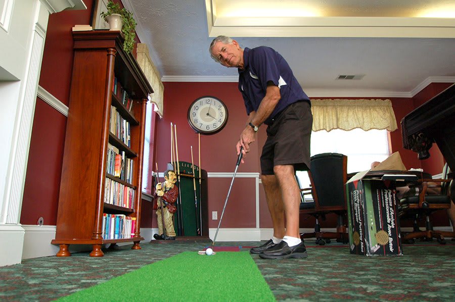 A person practicing their putting skills indoors on a green carpet.