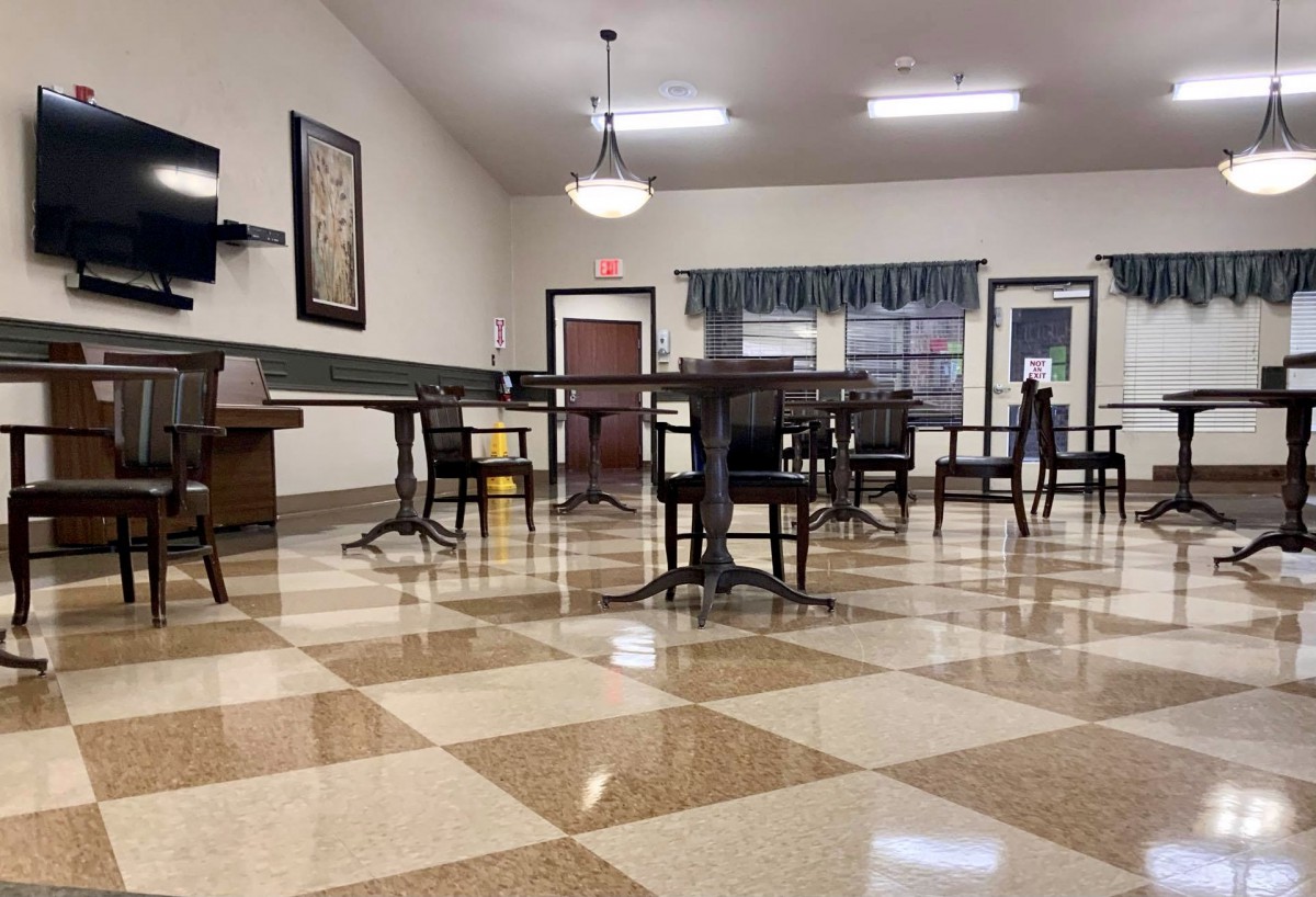 An empty dining area with checkered floor tiles and neatly arranged tables and chairs.