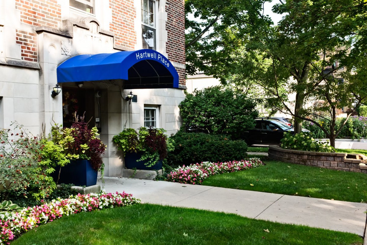 A well-maintained building entrance with a blue awning and landscaped greenery.