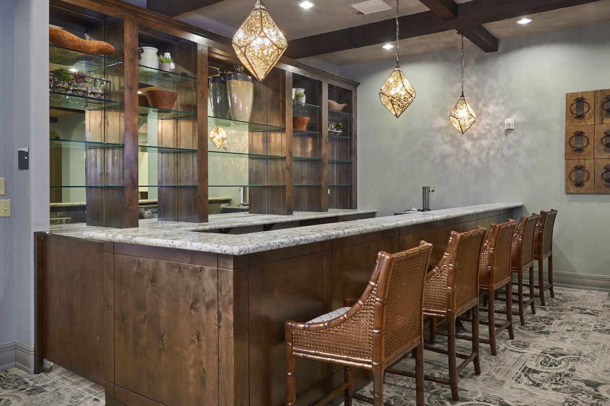A modern bar interior with a wooden counter, stylish chairs, and elegant pendant lighting.