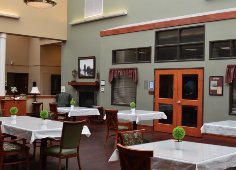 A spacious dining area with neatly arranged tables and chairs, featuring decorative elements and large windows.