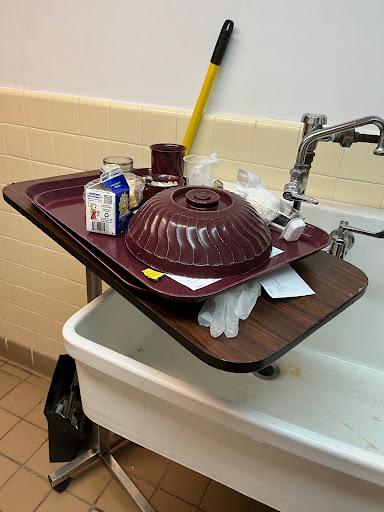 A piled-up tray with food containers balanced on a sink, illustrating a cluttered kitchen space.