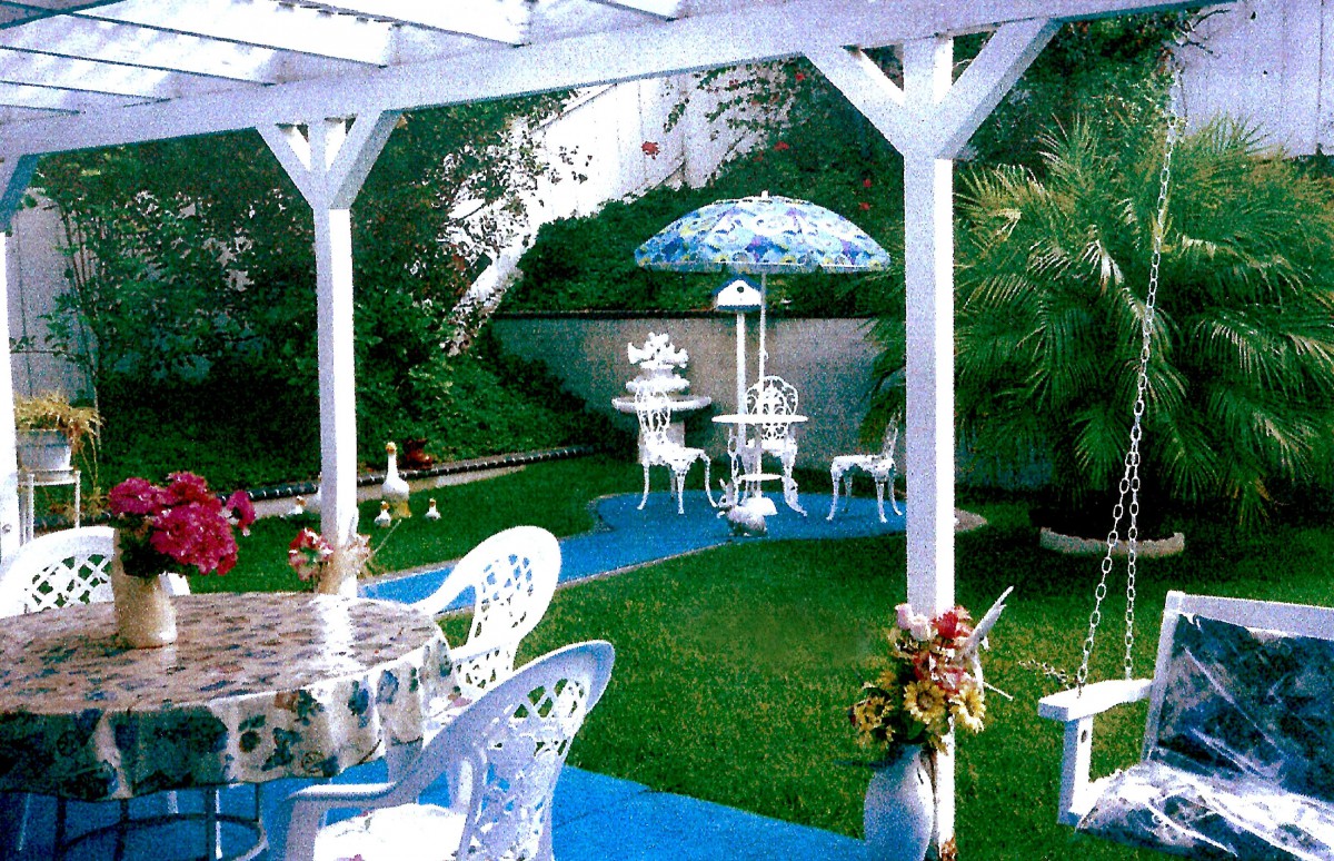 A picturesque garden setup with tables, chairs, and a decorative umbrella amidst lush greenery.