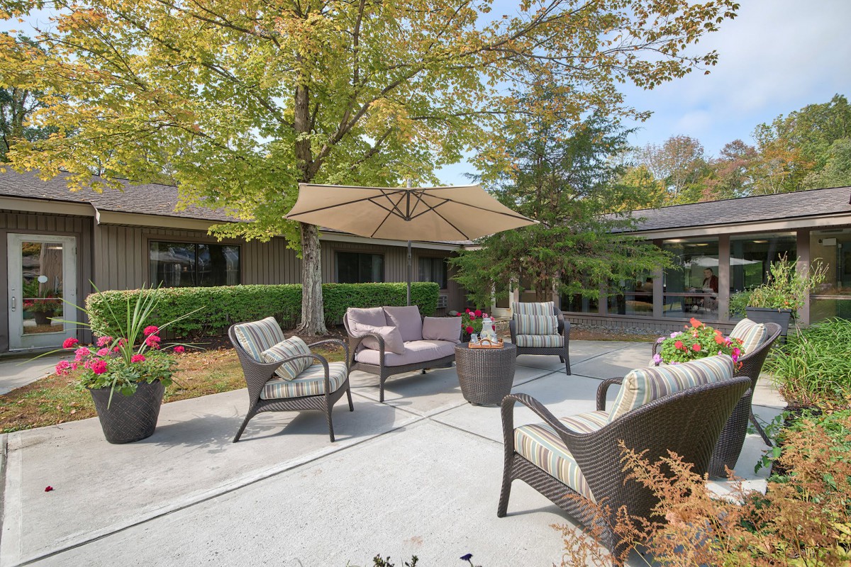 A cozy outdoor patio area with comfortable seating and a large umbrella, surrounded by lush greenery.