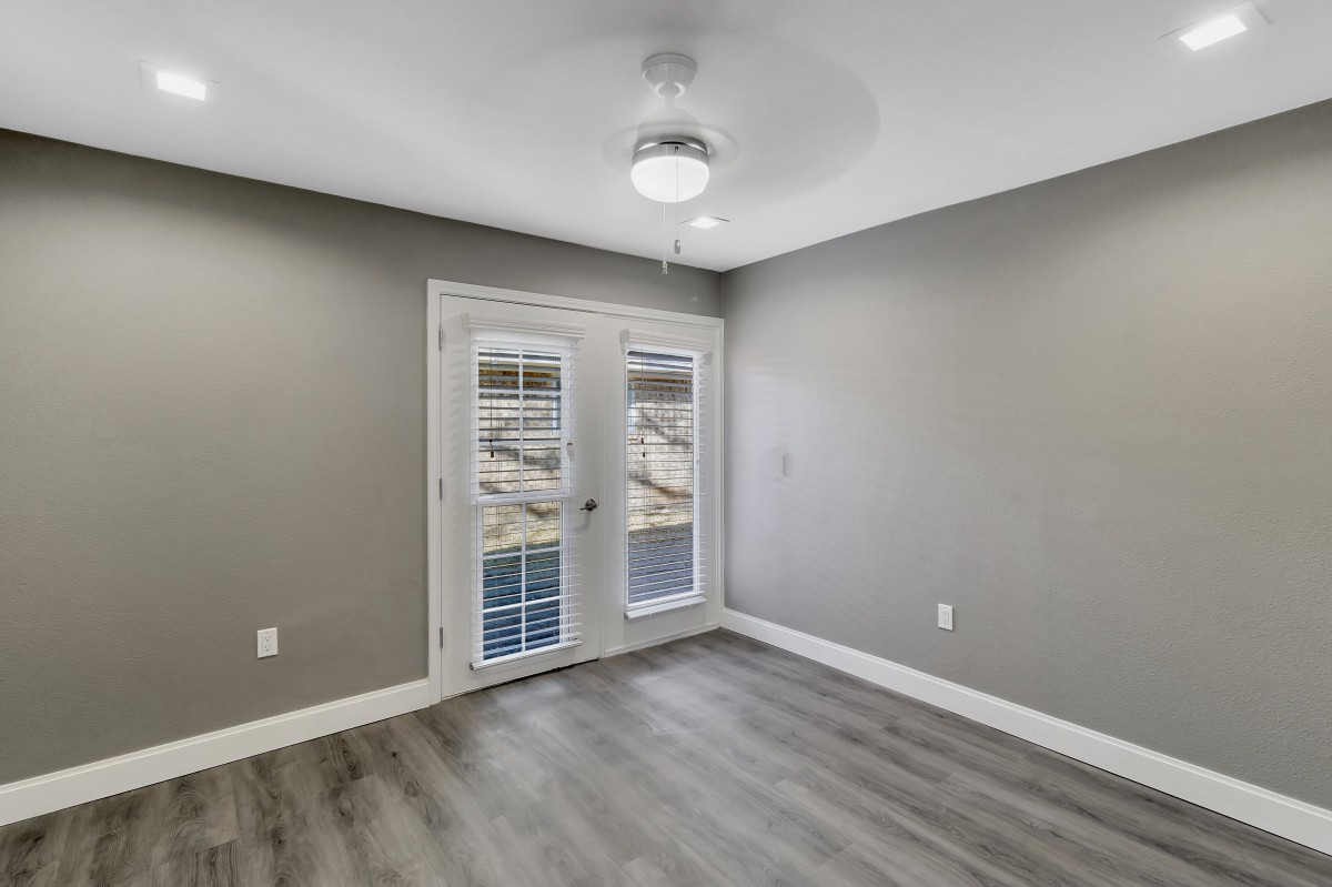 An empty room with gray walls, a ceiling fan, and a large windowed door.