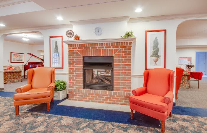 A cozy living room with a brick fireplace flanked by two orange armchairs and decorative artwork.