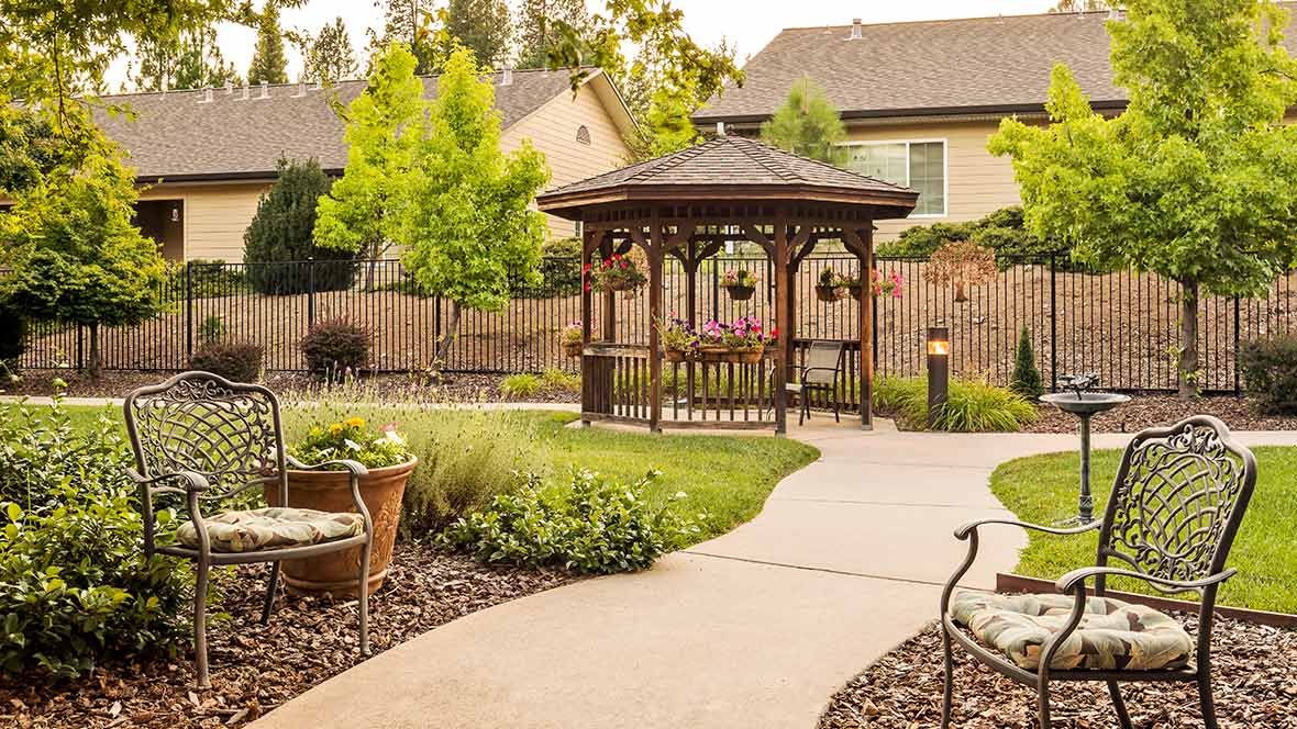 A picturesque garden featuring a wooden gazebo surrounded by lush greenery and a winding pathway.