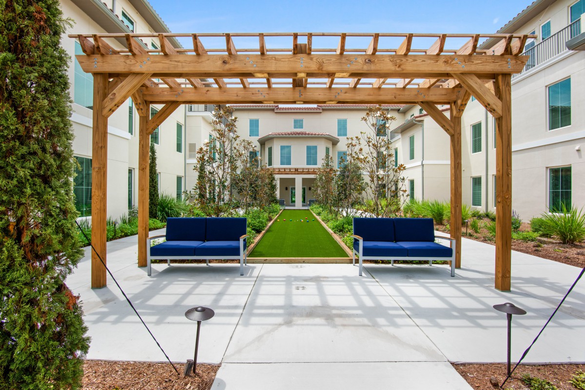 A well-designed courtyard featuring a pergola with blue benches and lush landscaping in front of an elegant building.