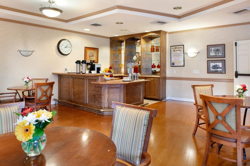 A cozy dining area with a coffee station, featuring wooden tables and chairs on a hardwood floor.