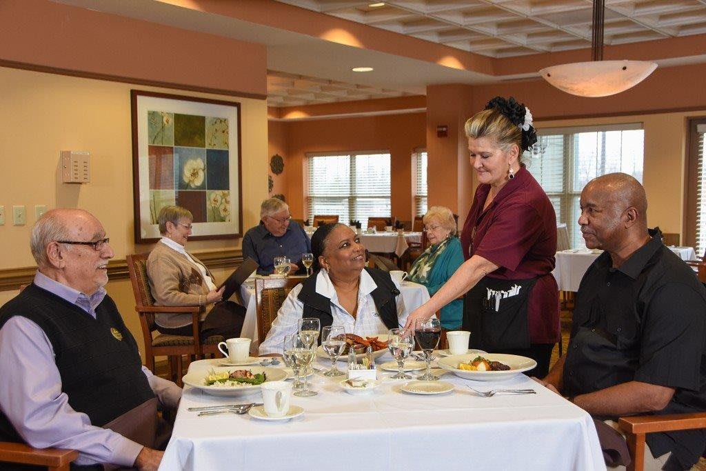 A waitress serves a group of elderly individuals enjoying a meal at a restaurant.