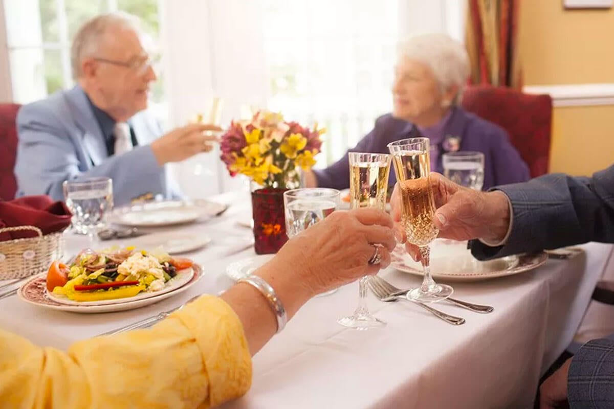 Elderly individuals enjoying a celebratory meal with a toast at a formal dining table.