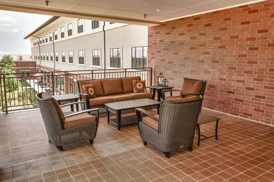 A cozy outdoor patio with a wicker furniture set, including chairs, a sofa, and a coffee table, against a brick wall backdrop.
