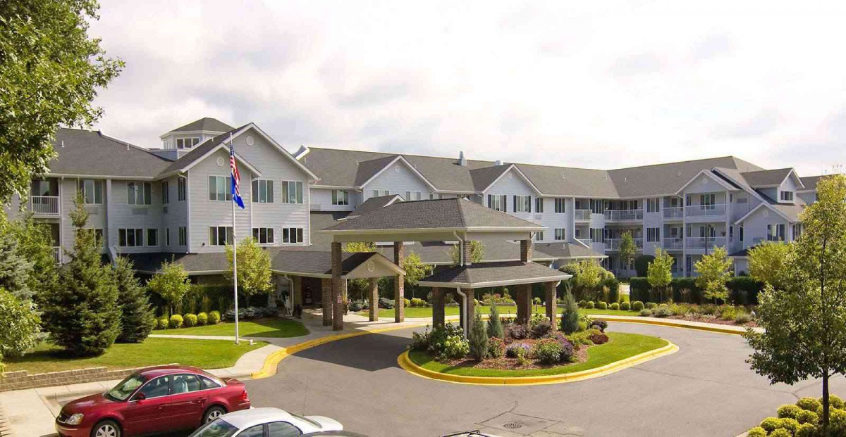 A large residential building with a landscaped entrance and driveway, featuring flags in the foreground.