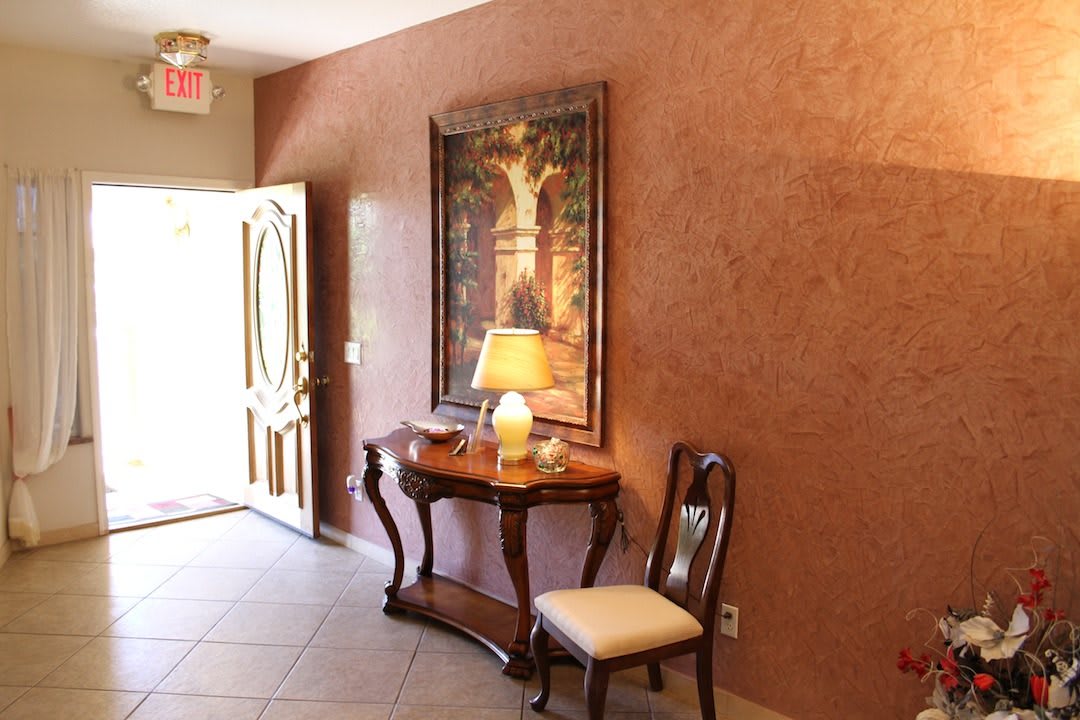 A warmly lit entryway featuring a wooden table with a lamp, a chair, and a decorative painting on the wall.