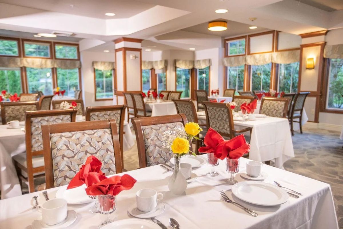 A beautifully arranged dining room with elegantly set tables, featuring red napkins and floral centerpieces.