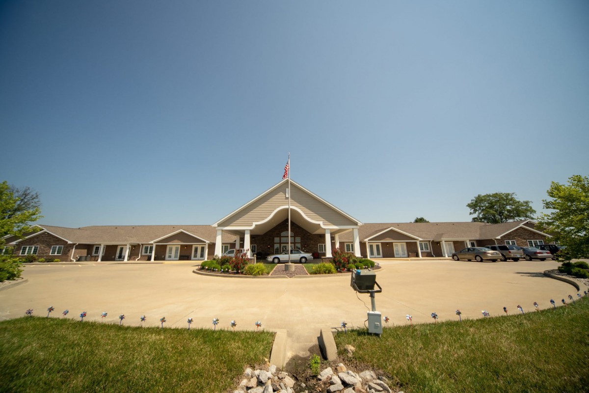Exterior view of a large symmetrical building with a prominent entrance, surrounded by a landscaped area and parking lot.