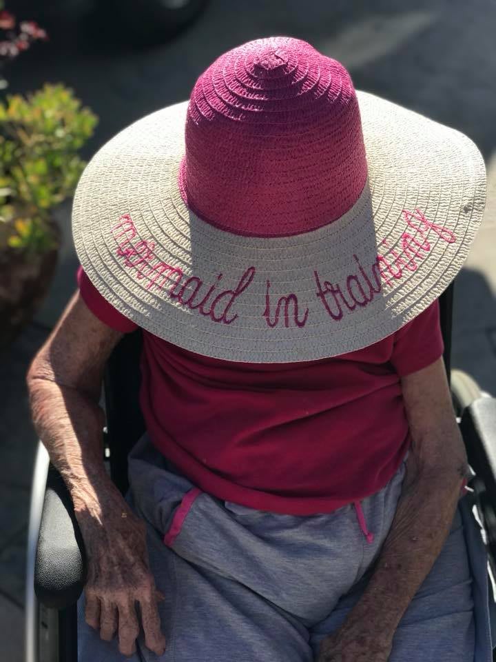 A person sitting in a wheelchair wearing a large sun hat with text and a red shirt.