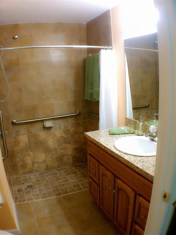 A small bathroom featuring a walk-in shower with a curtain, a sink with a wooden vanity, and tiled walls and floor.