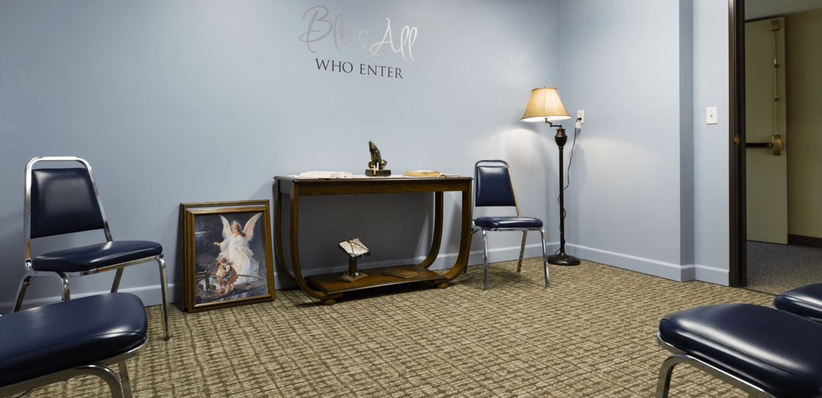 A small waiting room with a table, chair, artwork, and lamp providing a cozy atmosphere.