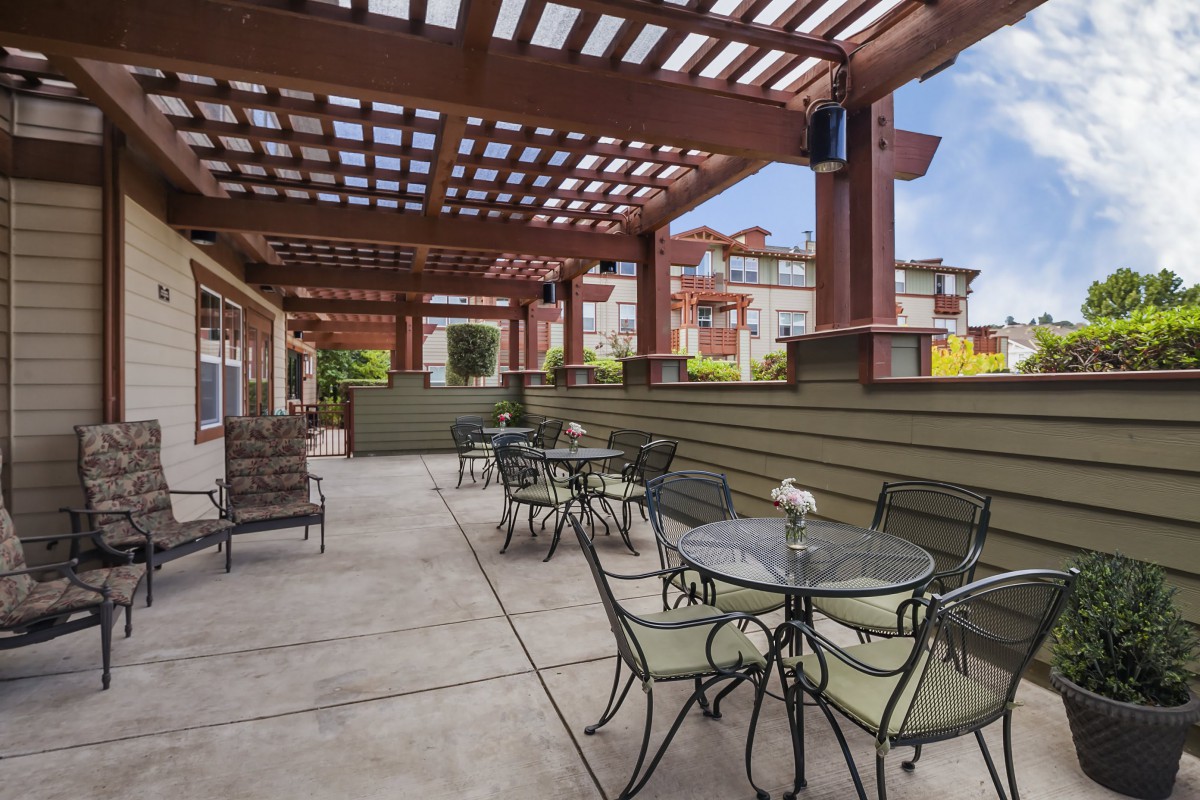 A spacious outdoor patio with tables and chairs under a wooden pergola.