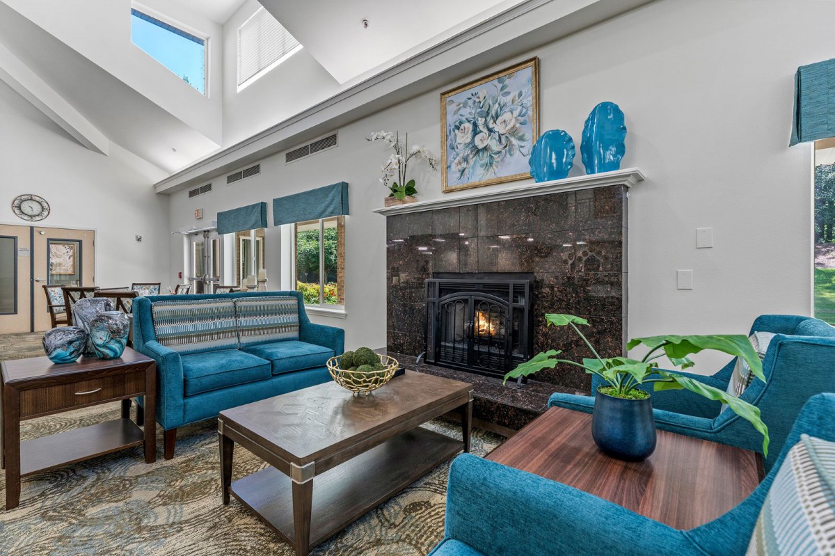 A modern living room featuring blue furniture and a cozy fireplace, highlighted by natural light from a skylight.