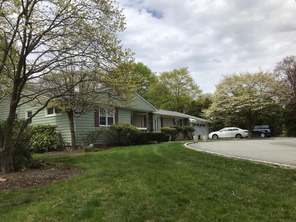 A suburban house with a well-maintained lawn and driveway, surrounded by trees.