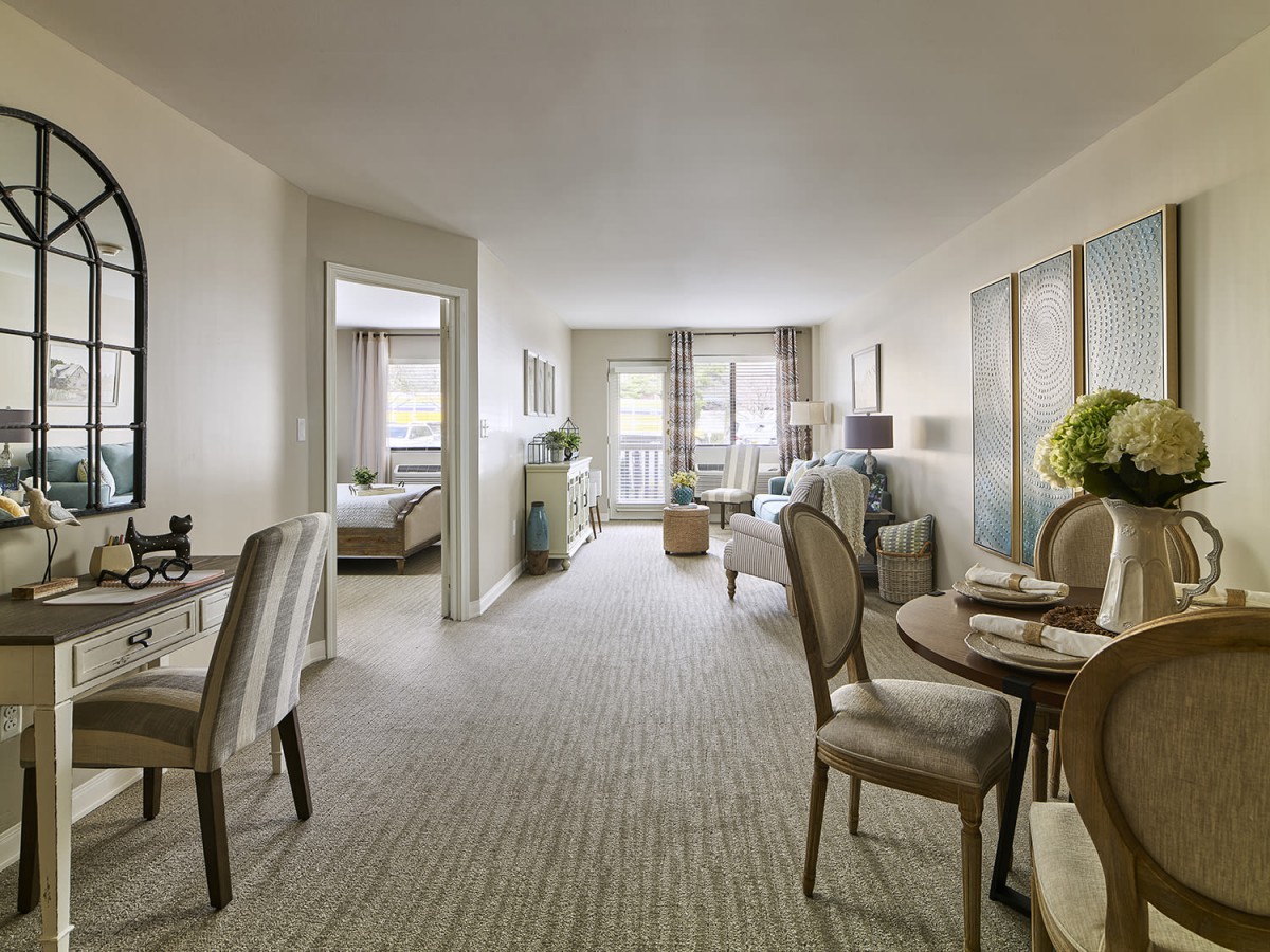 A modern apartment interior with a living and dining area, featuring elegant furniture and a carpeted floor.