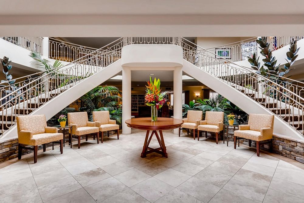 A beautifully designed lobby featuring a central table with flowers, surrounded by chairs and a grand staircase.