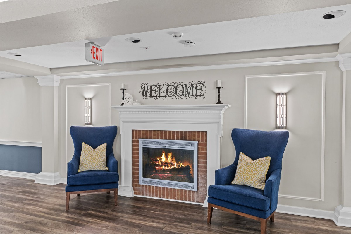A cozy living room with a fireplace, featuring blue chairs and a 'Welcome' sign.