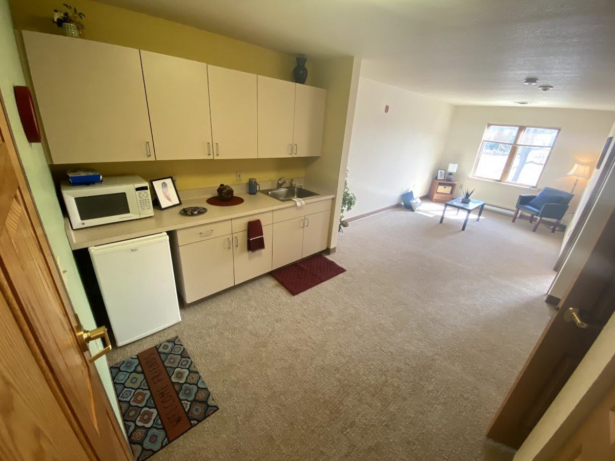 A compact kitchen area opens into a spacious living room with natural light streaming through the window.
