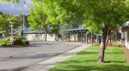 A building surrounded by trees with a sidewalk and parking lot.